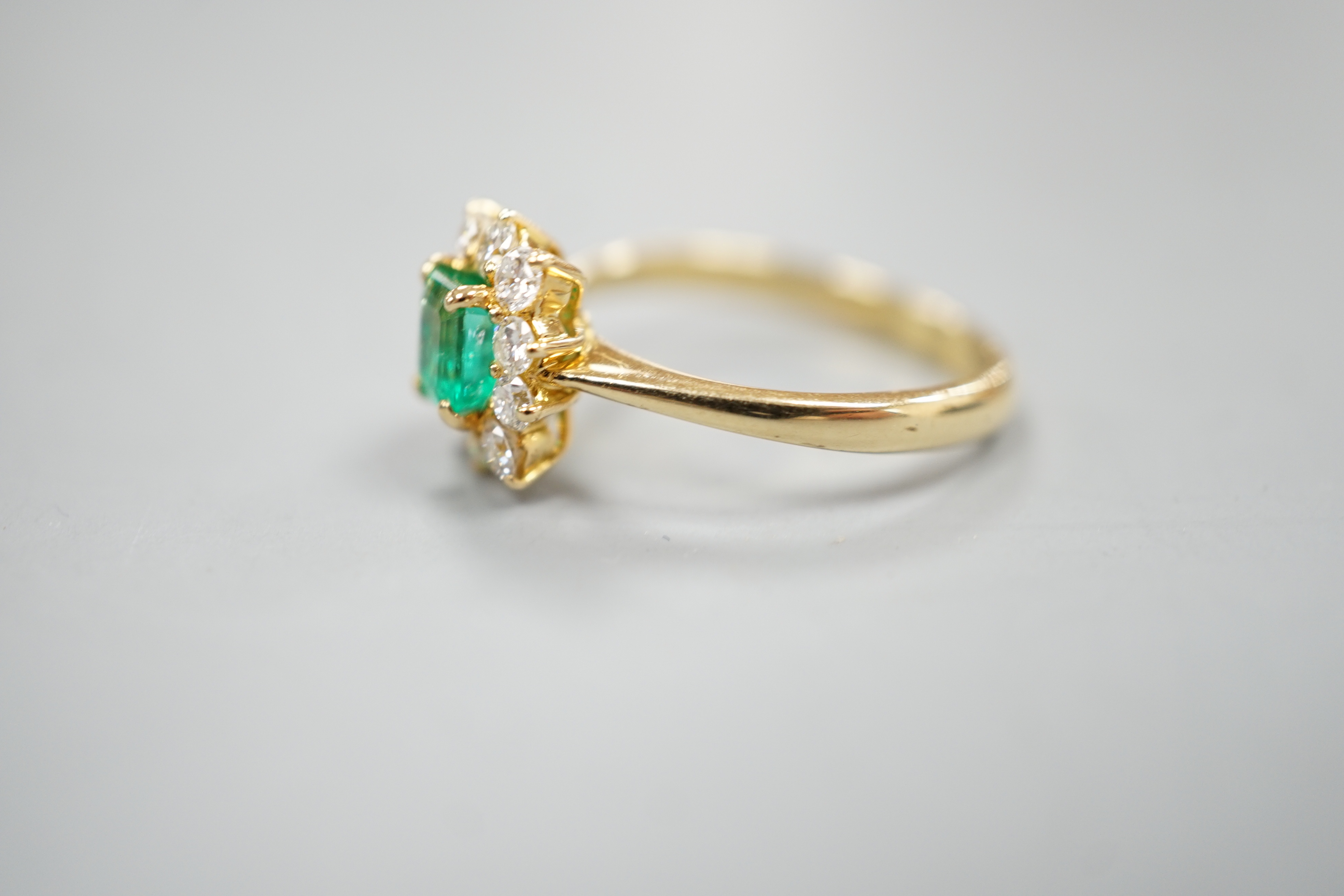 A 750 yellow metal, emerald and diamond set cluster ring, size m, gross weight 3.2 grams.